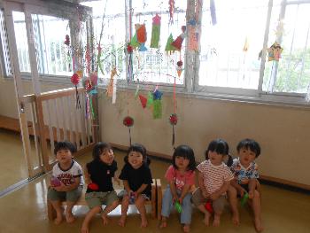 写真：色とりどりの笹飾りの前に座る6人の子どもたち