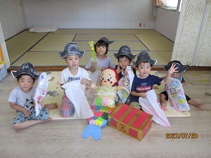 写真：人魚のぬいぐるみを助け出し、宝物を手にポーズをする子どもたち。頭には、自分で作った海賊帽子を被っています