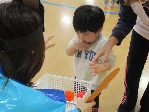 写真：おだいりさま役の保育者が持っているかごに、ひなあられに見立てたビニールボールを入れる1歳児の男児