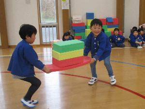 写真：ひしもちに見立てた3色のソフト積み木を協力して運ぶ2人の年長男児