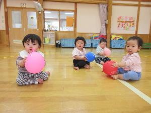 写真：お遊戯室でひよこ組4人の子どもたちが風船遊びをしているところ