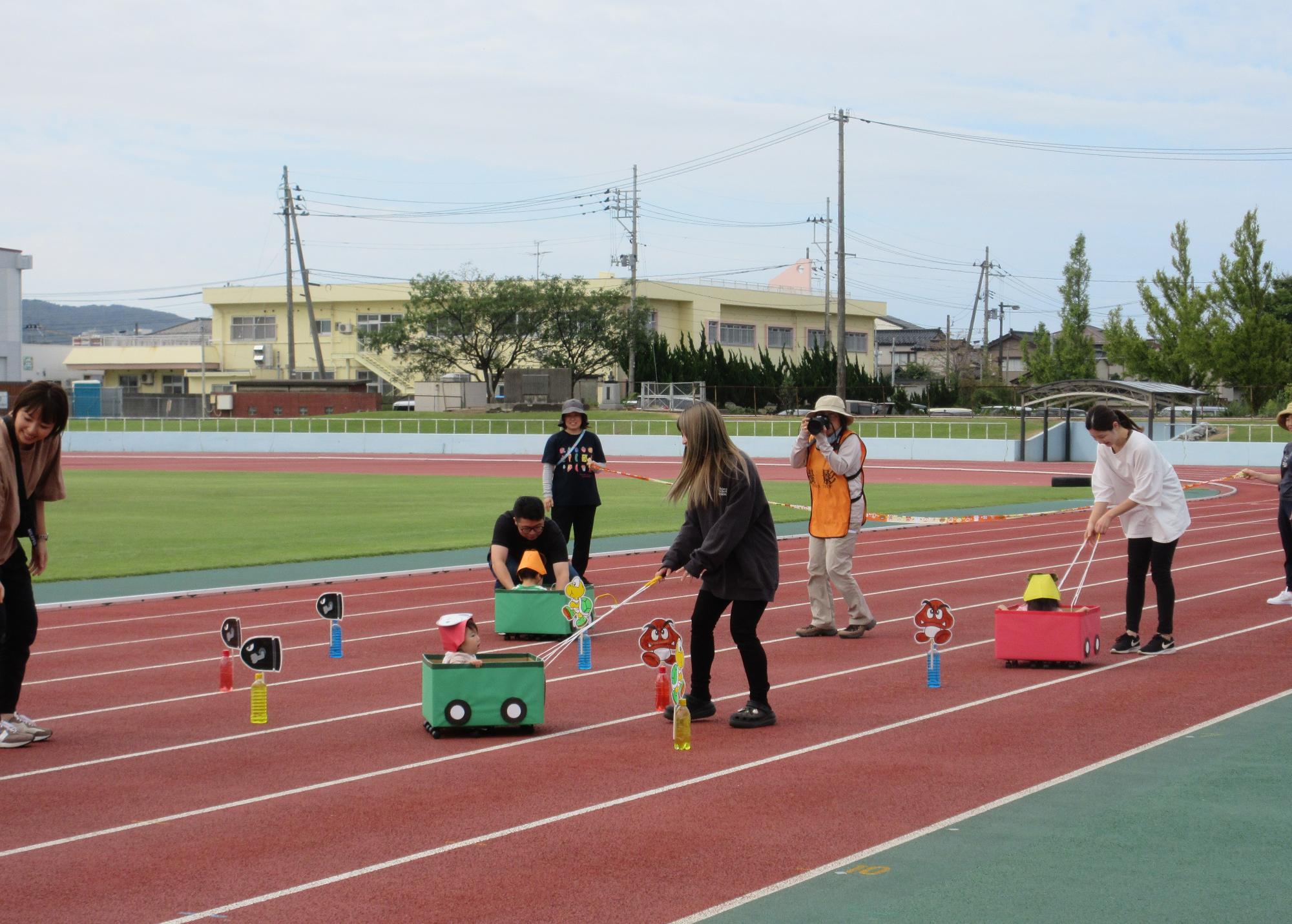 写真：ひよこ組の子どもが段ボール製のカートにのり、保護者にひもで引っ張ってもらっている様子