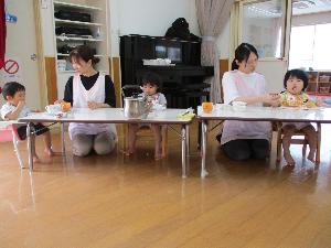 写真：保育士が付き添い、遊戯室でカレーを食べているひよこ組の子どもたち