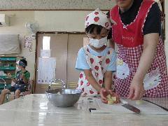 写真：エプロンと三角巾を付けたぞう組の女児が、包丁で切ったジャガイモをボウルに移そうとしています。