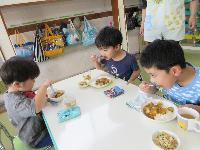 写真：3人の園児が自分達で作ったカレーを大きく口を開けて食べています