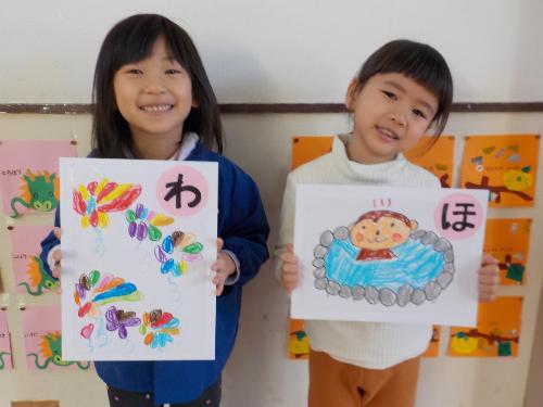 自分たちで描いて作ったジャンボカルタを持って微笑む年長児の女の子二人