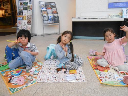 写真：博物館の1階でシートを敷いてお弁当を食べる3人の4歳児