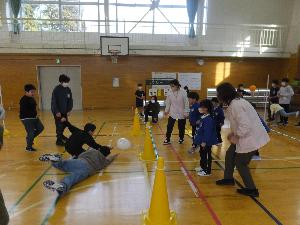 写真：新道小学校の体育館で保育園児数名と小学生数名が風船バレーで対戦しているところ。小学生2人が床につきそうな風船の下に滑り込んでいます