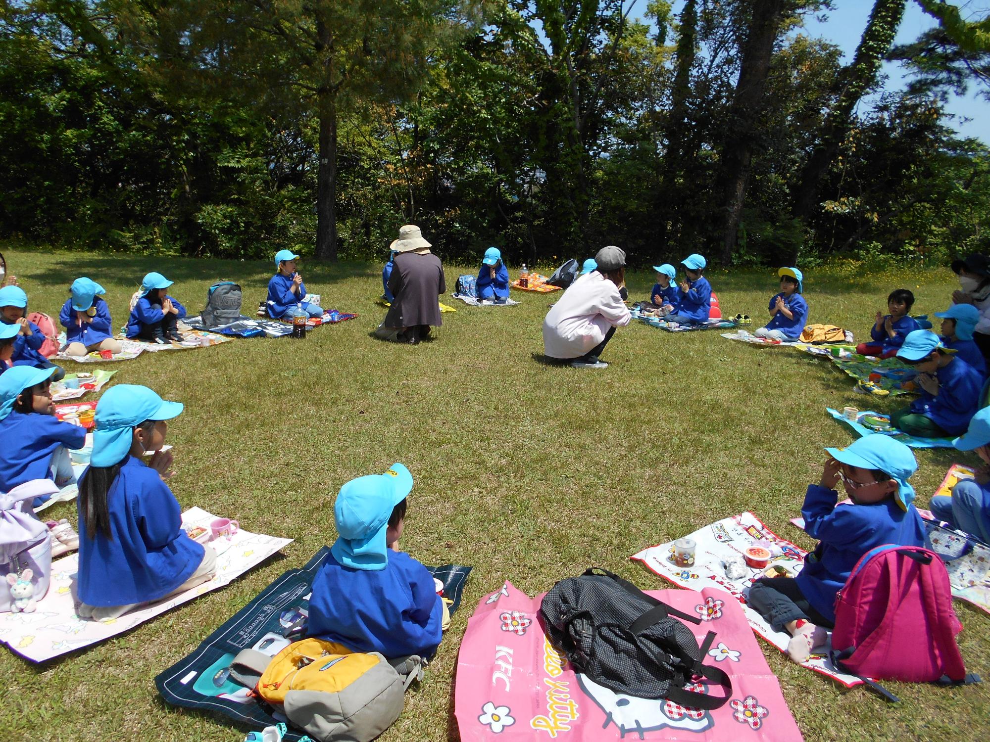 きりん組の子ども達が芝生の上にシートを広げ、お弁当食べる準備をしている写真