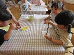 写真：小さな手に絵筆を持ち、黄色の絵の具を紙につけている子どもたち。