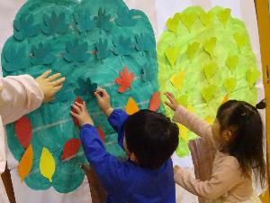 ポスターに貼られた緑色の葉を裏返して、裏面の赤や黄色に貼り替えようとする3歳児の写真
