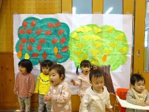 0、1歳児が、赤や黄色の葉が貼られた木のポスターの前で記念撮影をしました。