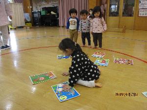 写真：1歳児と2歳児がカルタ取りをしています。2歳児女児はこいのぼりのカルタをとろうとしています。