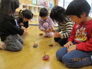 写真：保育室の床に正座し、コマを回す4歳児男児と3歳児女児たち