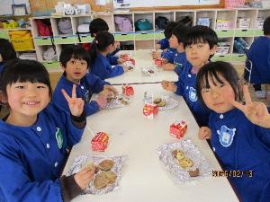 テーブルの上に置かれている自分で作ったクッキーをおいしそうに食べピースをしている年中児と年長児