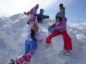 写真：園庭の雪山に登り上から眺めを楽しむ5歳男児。手にスコップを持つ5歳児女児もいます