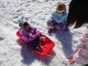 写真：雪が積もった園庭で、職員が引っ張るソリに乗る0歳児