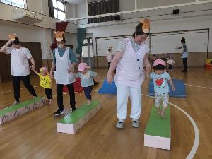 写真：保育士と手をつなぎながら、細長い板の上を歩くうさぎ組の子どもたち。