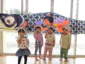 写真：遊戯室に展示してある鯉のぼりのまごいの前で、新聞紙で作った兜をかぶったうさぎ組の子ども達が並んでいるます