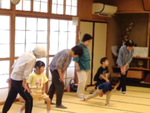 写真：年長児が地域の方と一緒にコツコツ貯筋体操をしている様子。片足を前に出し、ゆっくりと体重をかけています