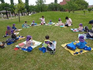写真：駅前公園の芝生広場でレジャーシートを広げ、お弁当を食べるぞう組の子どもたち