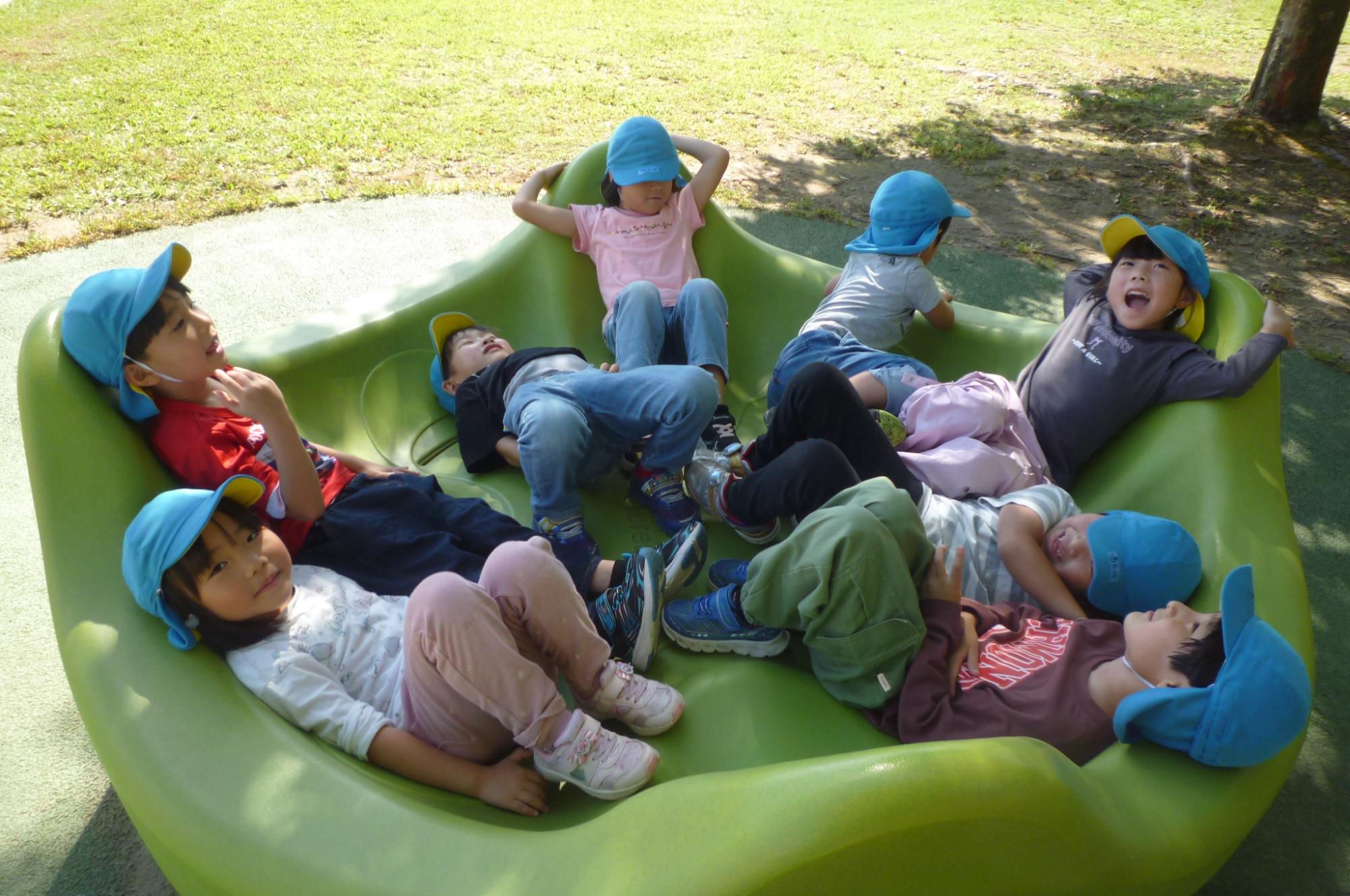 写真：8人の子どもたちがでこぼこした円形の遊具に座ったり寝転んだりして楽しんでいます