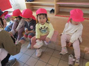 写真：玄関の上がり框に腰掛け、自分で靴を履こうとしているうさぎ組2歳児