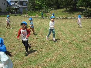 写真：青帽子をかぶったきりん組3・4歳児の子どもたちが公園でかけっこをしているところ