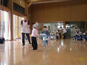 写真：新聞紙で作ったかぶとをかぶり、ぱんだ組の男の子と女の子の2人組が協力して、フラフープの網にかしわ餅をのせて運ぶゲームをしています