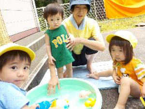 写真：水を張ったたらいにおもちゃを浮かべて、水遊びを楽しむ3人の0～1歳児