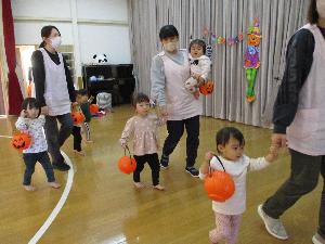 写真：保育者と手をつなぎ、カボチャ探しゲームに参加する0・1歳児