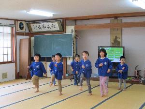 写真：地域の集会所でつながリズム体操を踊る3・4・5歳児。大きく腕を振って、足踏みをしています。