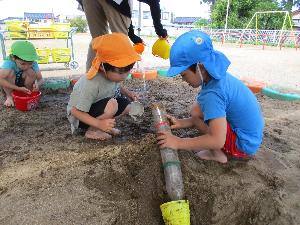 写真：ペットボトルを繋げて、砂場で水路を作る2人の男児