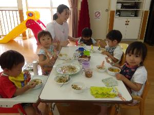 写真：テーブルを囲んでカレーライスを食べるりす組5人と保育士