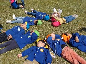 写真：9人ほどの子どもたちが芝生の上で大の字になって寝転がっています。
