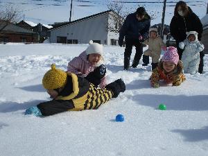 写真：雪上でカラーボールを目指してほふく前進する1歳児数人