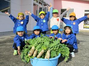 写真：収穫した大根を前に喜ぶ8人の子どもたち
