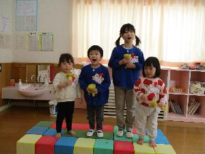 写真：ソフト積み木でできたステージに上がって、マイクを片手にお題の歌を熱唱する園児4人