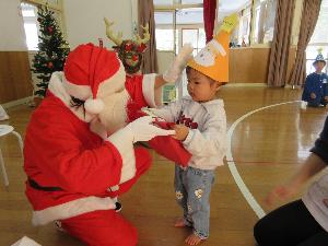 1歳児1名がサンタクロースからプレゼントを受け取っています。