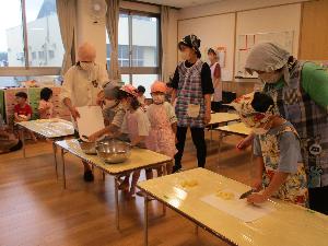 写真：職員と一緒にジャガイモを切る男の子と切ったものをボウルに入れている年長児の男女