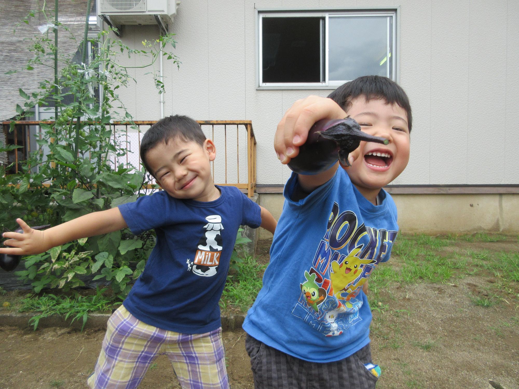 写真：こあら組の2人の子どもが、大きなナスを手にして、満面の笑みを浮かべています。