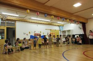 遊戯室で子ども達が1列に並んで保護者の前で踊りを披露しているところ