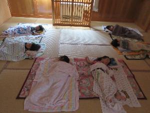 写真：薄暗くした保育室で布団を並べ、お昼寝をしている子どもたち