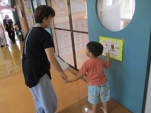 写真：祖母と手をつなぎ、掲示してあるクイズを指さす3歳児男児