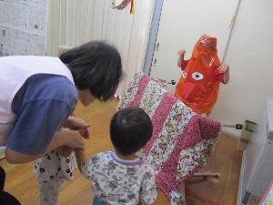 写真：からかさお化けに変身した5歳児が、机の陰から飛び出し、2人の1歳児を優しく驚かしています