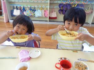 写真：カレー皿を左手に持ち大きく開けた口にスプーンでカレーライスを運ぶ2人の園児。