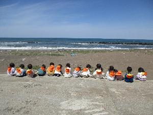 砂浜で、海に向かって2歳児と3歳児が横一列に座っている後姿の写真
