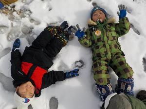 写真：雪の上に寝転がり笑顔を見せるぱんだ組の2人の子ども