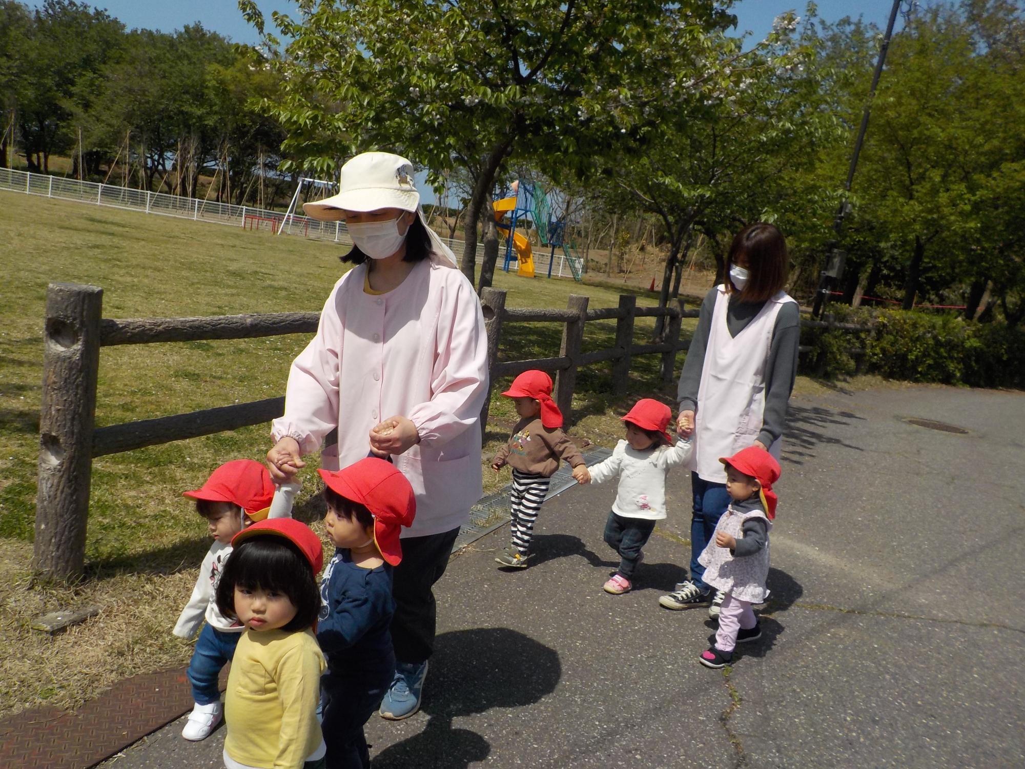 写真：子どもたちが保育士と手をつないで散歩をしているところ