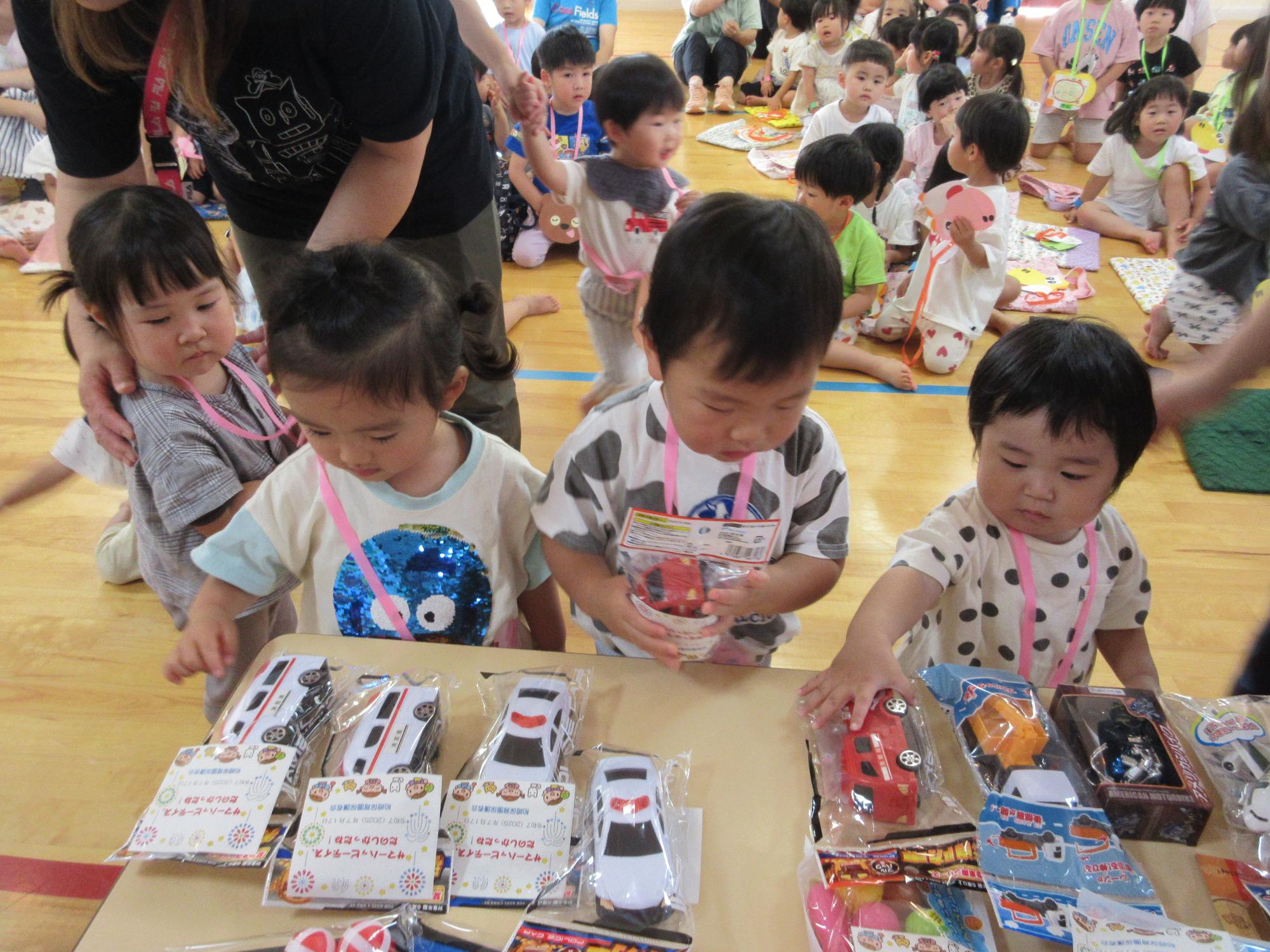 写真：テーブルの上に並んだ抽選会のおもちゃをじっくりと見定める1歳児4人